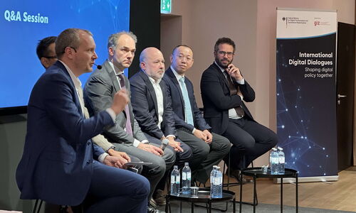 Five panelists are sitting on the stage looking right to the moderator sitting at the right end doing the introduction to the paneldiscussion
