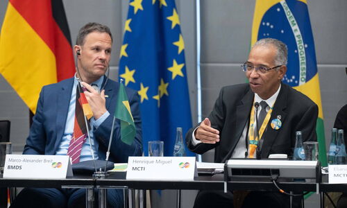 The photo shows Henrique Miguel from MCTI and Marco-Alexander Breit from BMDS, sitting in front of a German, Brazilian and European flag.