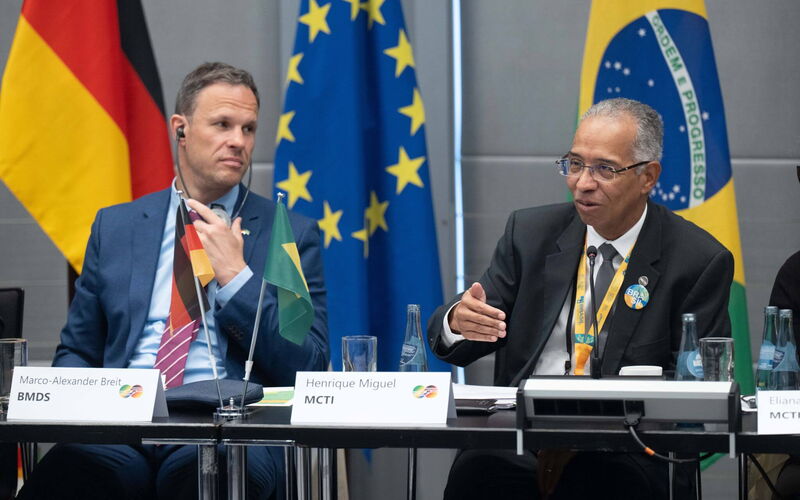 The photo shows Henrique Miguel from MCTI and Marco-Alexander Breit from BMDS, sitting in front of a German, Brazilian and European flag.