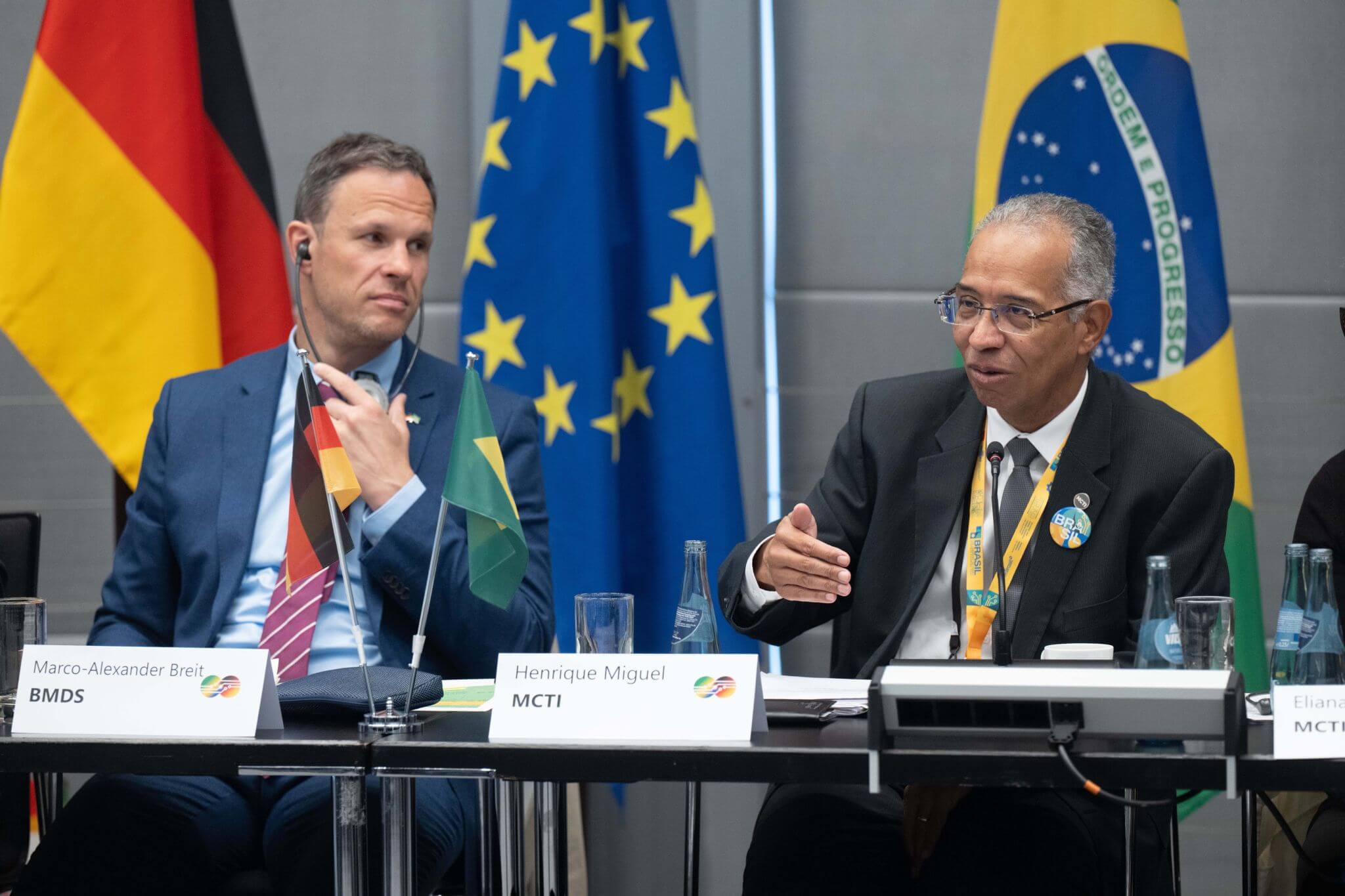 Das Foto zeigt Henrique Miguel vom MCTI und Marco-Alexander Breit vom BMDS vor einer deutschen, einer brasilianischen und einer europäischen Flagge.